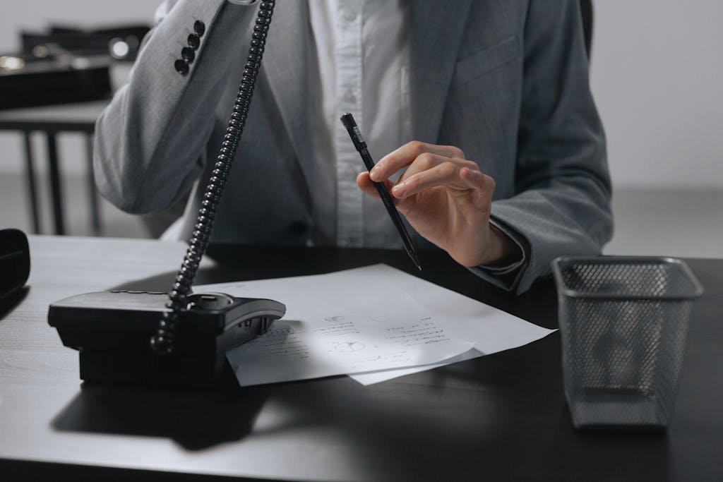 A business professional in a gray suit making notes with a pen while on a phone call.